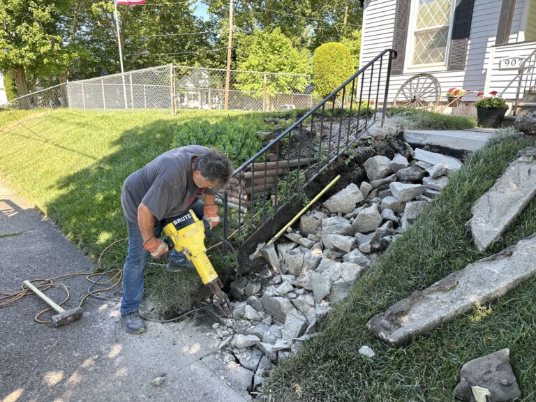 Contractor removing damaged concrete stairs and sidewalk with a jackhammer during residential stair replacement project.