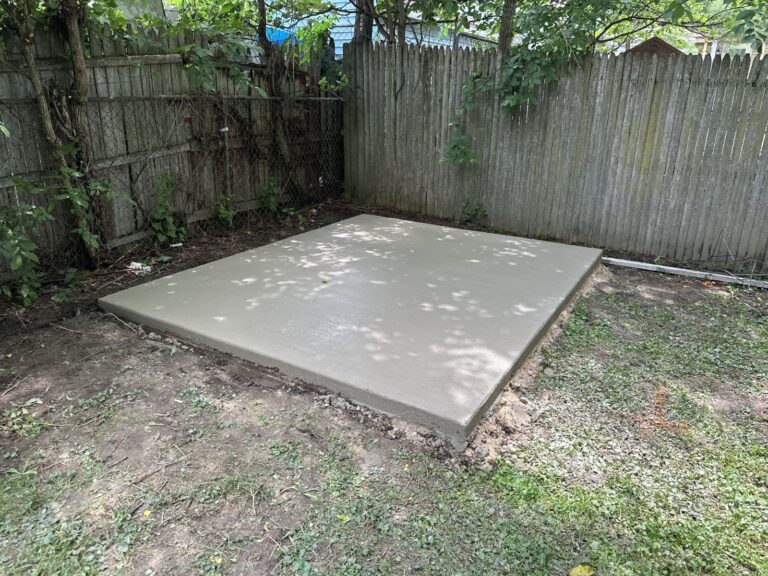 Completed concrete patio slab with smooth broom finish installed in backyard corner.